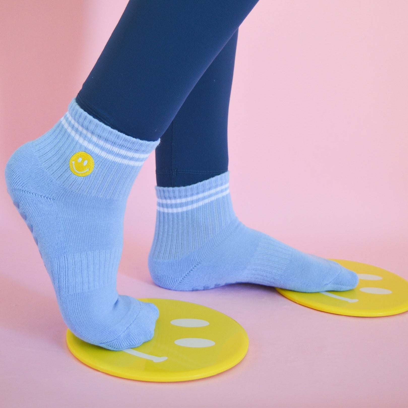 Person wearing light blue socks with smiley face designs with happy face sliding disks