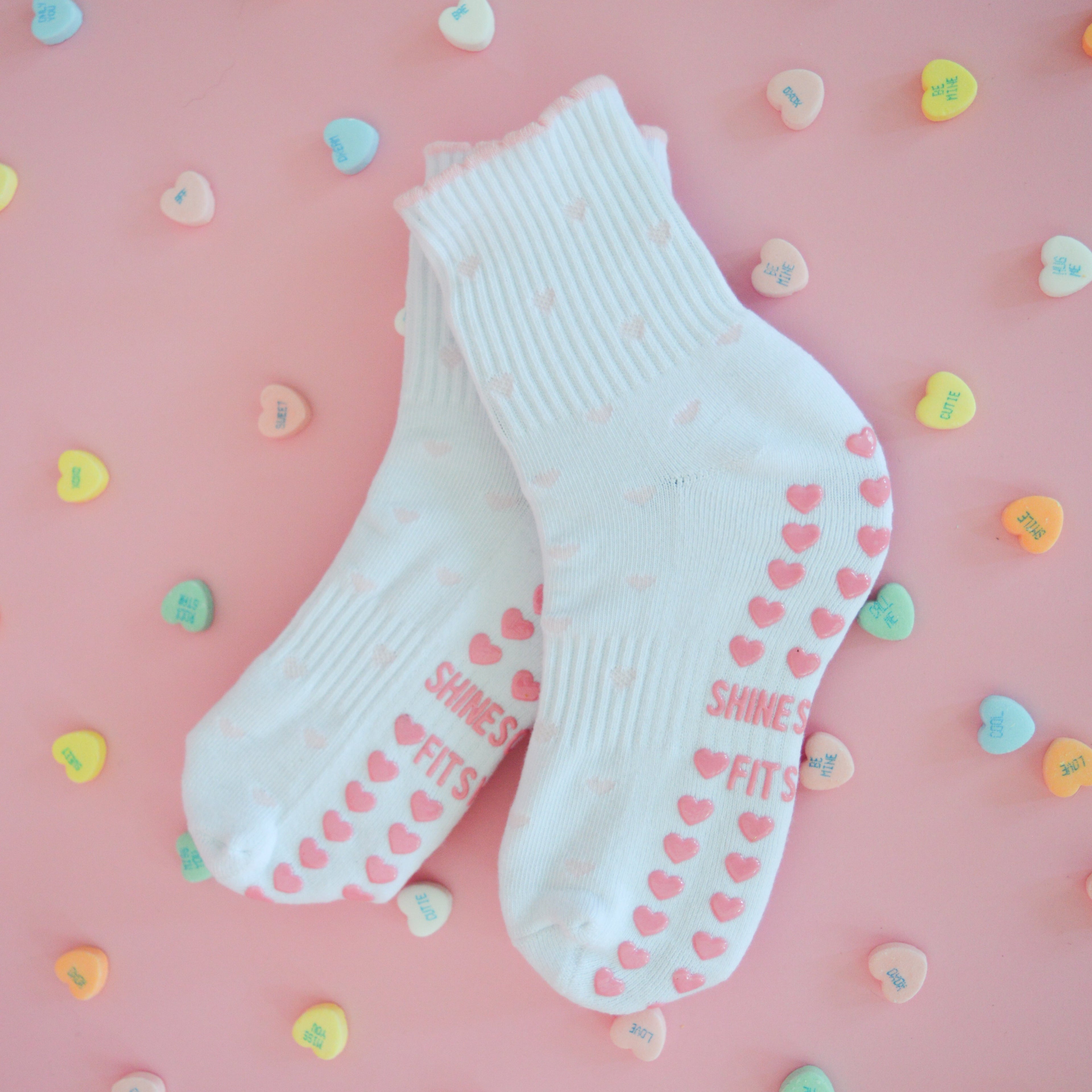 White socks with pink hearts on a pink background with colorful heart-shaped candies.