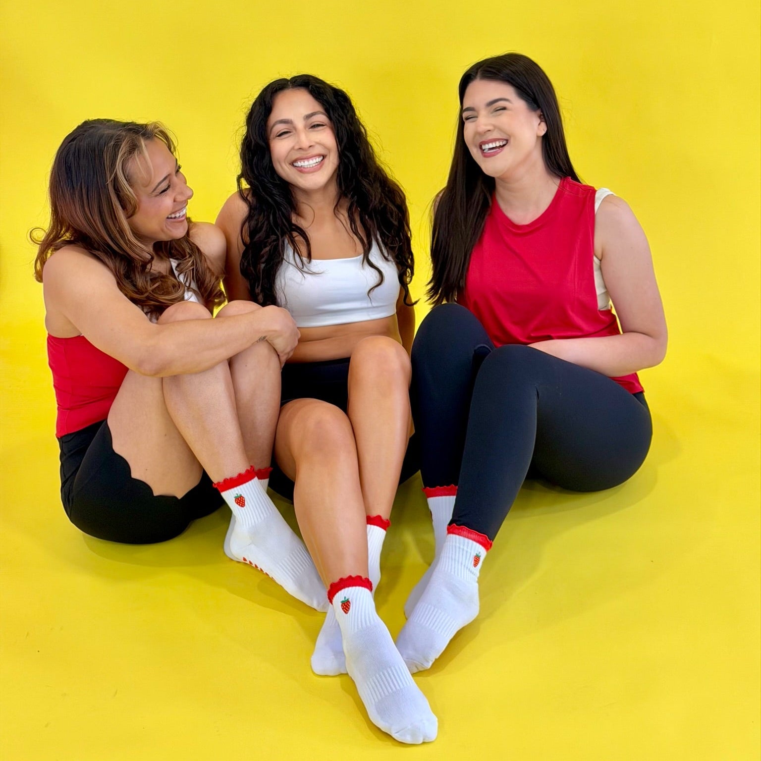 Three women sitting on a yellow floor wearing matching outfits with red and white accents.