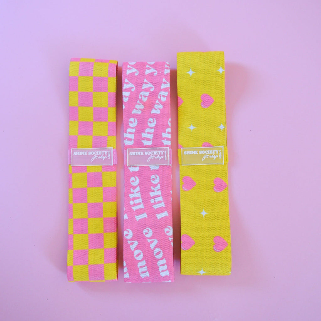 Three colorful hip bands with checkered and patterned designs on a pink background