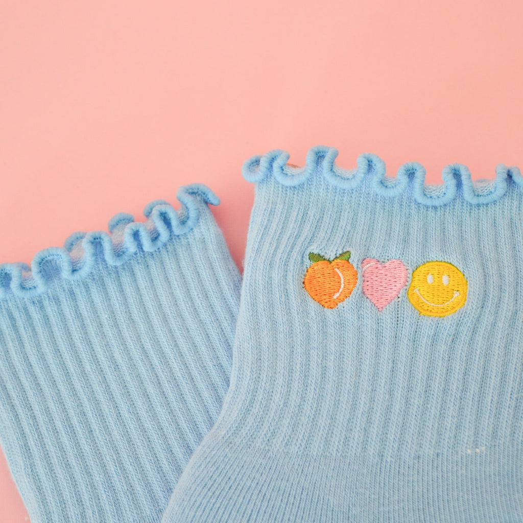 Light blue socks with ruffled edges and peach heart and happy face designs on a pink background