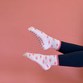 White socks with pink floral patterns worn by a person on a pink background